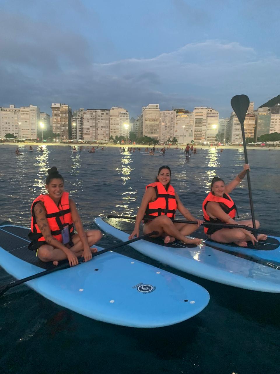Três amigas com coletes laranja sobre o mar ao entardecer