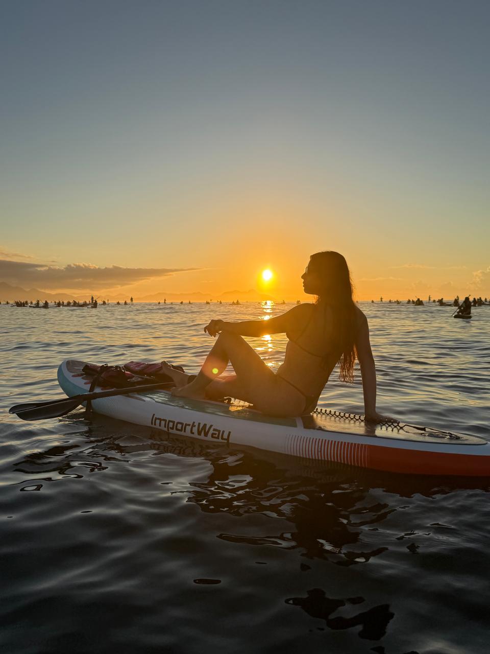 Mulher contemplando o sol nascente sentada no SUP